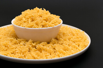 Uncooked Fusilli Pasta Lying on White Plate on Black Background. Raw and Dry Macaroni. Unhealthy and Fat Food