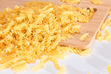 Uncooked Fusilli Pasta Scattered on Wooden Board and White Table. Raw and Dry Macaroni. Fat and Unhealthy Food
