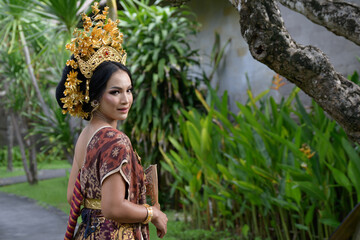 Young gorgeous woman in a beautiful batik costume with a crown and a Balinese garden