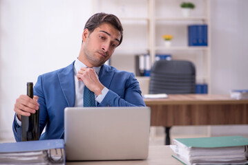 Young male employee drinking alcohol at workplace