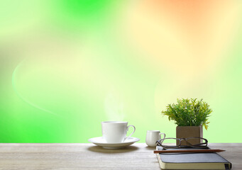 On the table, place a cup of white coffee Notebook (Diary) blue pen and glasses.
The garden has green trees. (Blur)