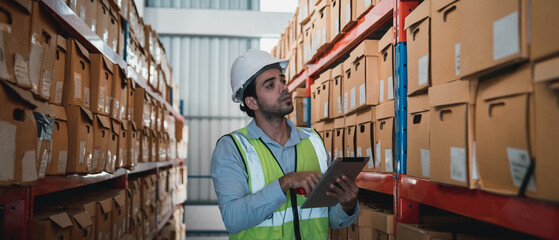 A worker in the warehouse uses a smart tablet to check the stock is on the shelves at the...