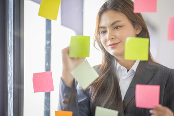 Business Asian female employee with many conflicting priorities arranging sticky notes commenting...