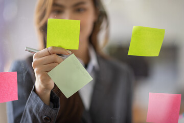 Business Asian female employee with many conflicting priorities arranging sticky notes commenting...