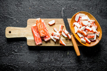 Pieces of crab sticks on a wooden cutting Board with a knife.