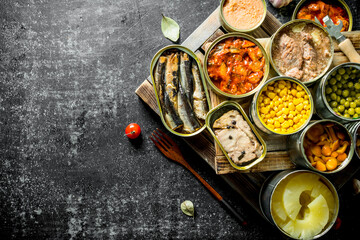 Various open tin cans with canned food on wooden tray.