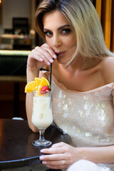 Fototapeta premium Sensual woman wearing a white cocktail dress drinking a tropical cocktail. Pina colada. Cocktail party.