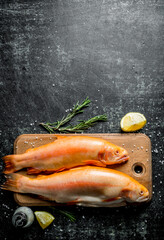 Raw fish trout on a wooden cutting Board with lemon slices and rosemary.