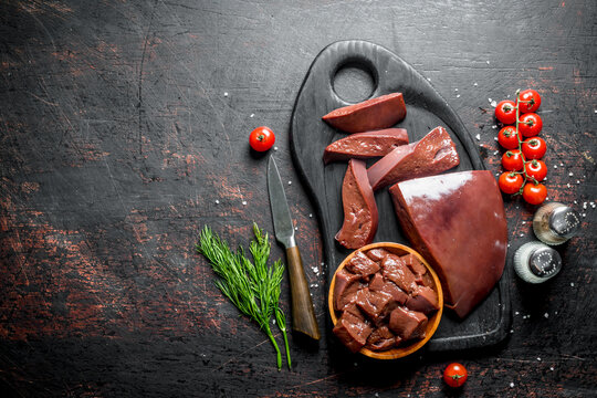 Raw liver with cherry tomatoes, spices and dill on a cutting Board.