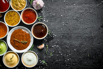 An assortment of different sauces in bowls on a stone Board.