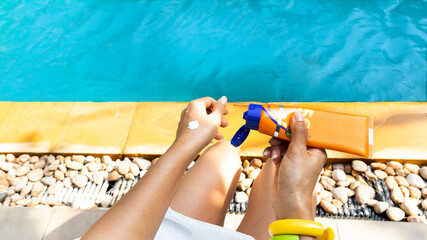 Middle age hand with sun cream on her legs. she is holding sunscreen bottle on the poolside as applying moisturizing lotion on skin.Skin care protection cpncept