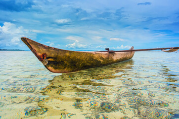 Wooden outrigger canoe anchored in a shallow tropical lagoon