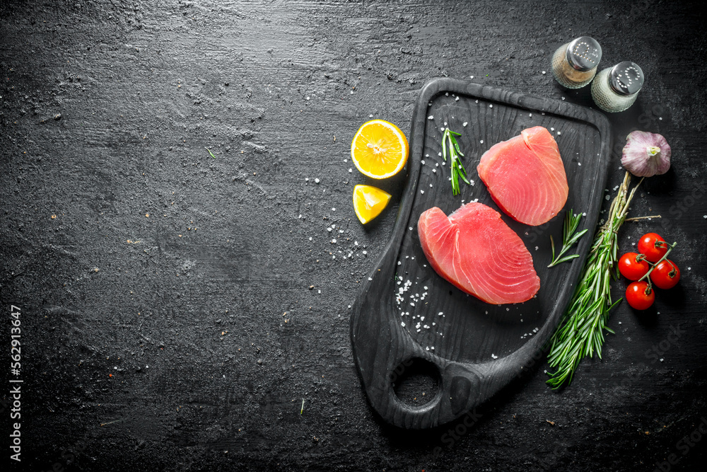 Canvas Prints Fresh uncooked tuna steak on a cutting Board with tomatoes, rosemary, garlic, spices and lemon.