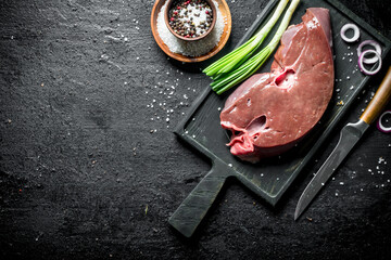 Raw liver on a cutting Board with a knife, spices and onions.