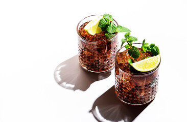 Rum cola cocktail with strong alcohol and ice, garnished with mint and lime in glass. White...