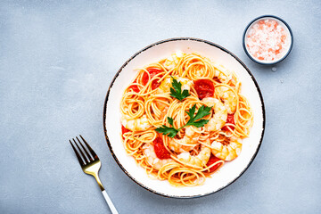 Spaghetti pasta with shrimp, cherry tomatoes, olive oil and parsley on gray table background. Top view, copy space