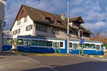 Fototapeta na wymiar Blue and white VBZ tram line 5 passing behind old protestant church at district Fluntern at City of Zürich on a blue cloudy autumn day. Photo taken December 8th, 2022, Zurich, Switzerland.