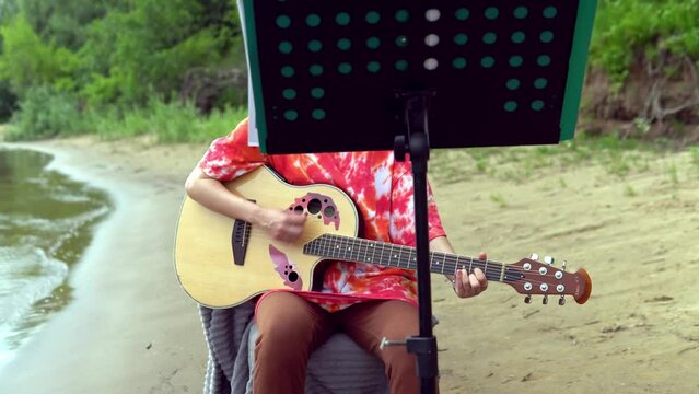 A young girl plays an acoustic guitar on the banks