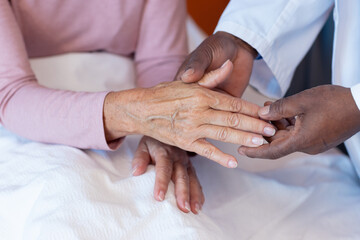 Midsection of diverse senior male doctor examining hand of senior female patient on bed, copy space