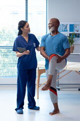 Vertical of diverse female physiotherapist and senior male patient holding leg, copy space