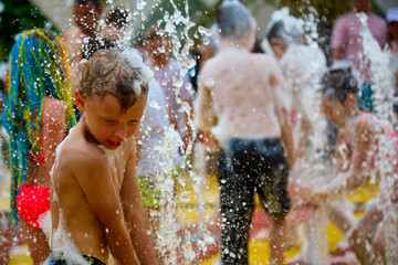 Little boy plays on the playground between the jets of water in the fountain on a sunny summer day. Active summer holidays for children in the popular city water amusement park