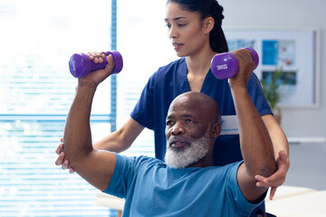 Diverse female physiotherapist helping senior male patient exercise with dumbbells - obrazy, fototapety, plakaty