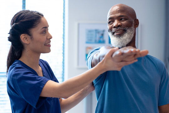 Smiling Diverse Female Physiotherapist Treating Arm Of Senior Male Patient, Copy Space