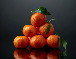 Tangerines or clementines with green leaves on a black background.
