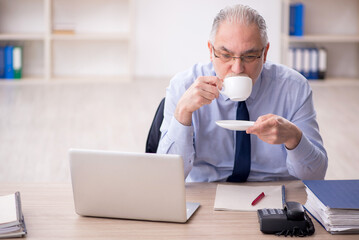 Old male employee drinking tea in the office