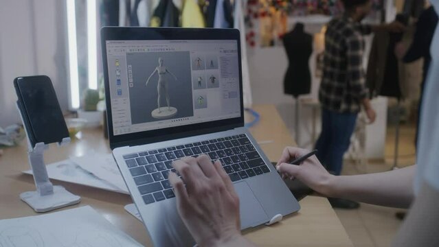 Female fashion designer develops future design of clothes in 3D modeling program on laptop using digital tablet and stylus. She works in atelier workshop. Fashion and technologies in business concept.