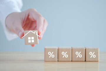 Percentage sign and hand holding house icon on wooden block. Refinance to reduce the interest of home loan. Mortgage, loan, repayments, credit limit, house tax, business and financial concept.