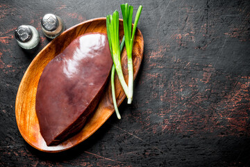 Raw liver on a plate of green onions and spices.