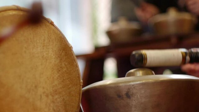 Skinned drum and south east Asian bonang gamelan continuously struck by mallets during live performance, filmed as close up.