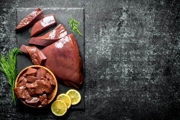 Pieces of raw liver on a stone Board with pieces of lemon. - 562926051