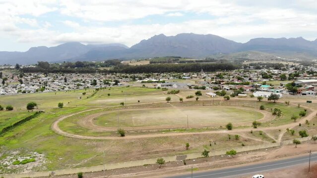 A drone shot of a township dirt athletics track in Paarl. The track is surrounded by a community of houses and edgy mountains as a backdrop.