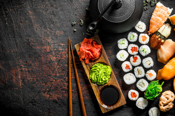 Different types of Japanese sushi, rolls and maki with sauce, wasabi and green tea in a teapot.