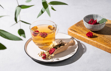 Herbal tea with pomegranate flowers in a glass cup on a plate on a white background with eucalyptus branches.