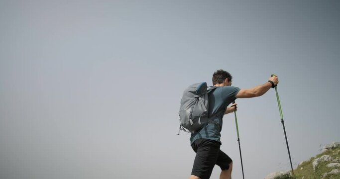 Hiker walking up a hill towards the red signpost with writen directions, partially clear sky.