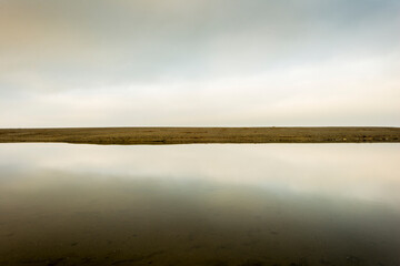 The sky reflects on a still pool of water.