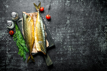 Whole smoked mackerel on a cutting Board with greens, tomatoes and spices.