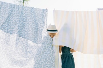 siblings hiding behind the washing drying on the line at home