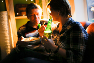 Mature couple drink beer from green beer bottles, dark style. Soft focus.