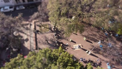 A dynamic aerial shot of dancing partners performing Tango within the public park. The footage has  a circular blur effect on it to emphasize the performing couples as the main subjects of this clip.