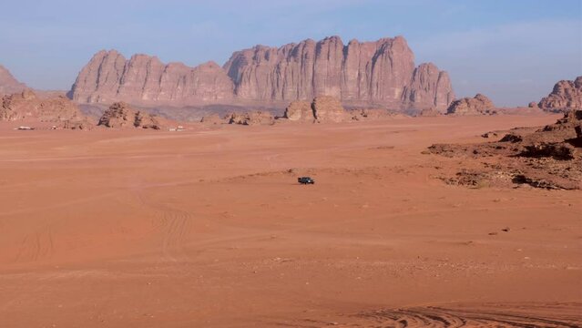 Solo grey 4WD truck driving across vast red sand desert in Wadi Rum with rugged sandstone and granite mountains in the distance in Jordan