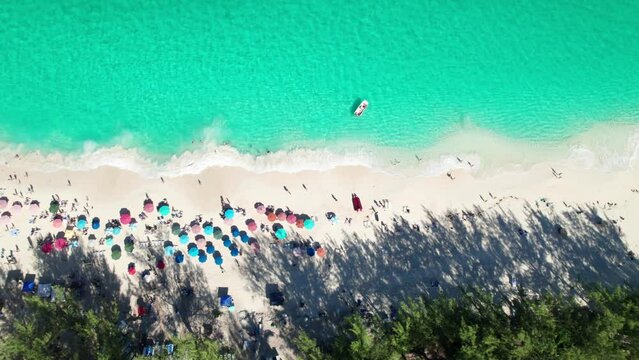 Overhead 4k drone clip of sandy beach with emerald water, crashing waves, colorful umbrellas.