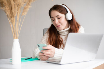 caucasian female enjoying music or podcast and holding smartphone.  Red hair woman in modern office