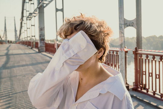 Close up woman hiding face behind shirt sleeve standing on bridge portrait picture. Closeup front view photography with blurred background. High quality photo for ads, travel blog, magazine, article