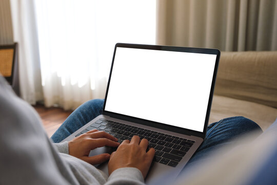 Mockup image of a woman working and typing on laptop computer with blank screen on sofa at home