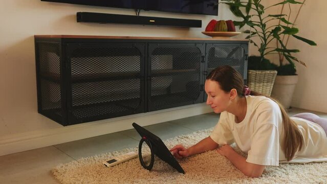 Student girl uses tab lying on the floor on furry carpet and switches on AC with heating mode.Fast and safe way to warm up room.Energy efficient and money saving heating solution.Stylish home. HQ 4k