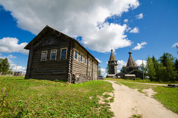 Fototapeta na wymiar A huge peasant house against the backdrop of a church and a bell tower. Russian North, Oshevenskaya volost